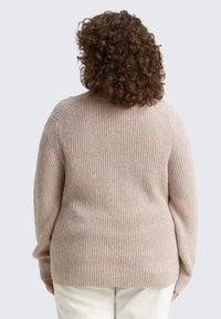 Pull en tricot rose clair avec une texture côtelée, doté de manches longues et d'un col rond, présentant des détails de couture visibles et une coupe décontractée.