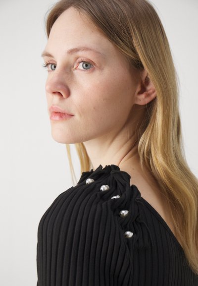 Black ribbed top with a fitted design, featuring pleated accents and silver button details on one shoulder. Soft, textured fabric.