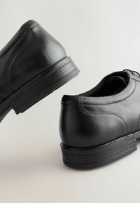 Zwarte leren schoenen met een gladde afwerking, een ronde neus en een lage rubberen hak, met subtiele stiksels en een vetersluiting.