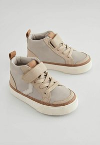 Baskets montantes beiges en tissu doux avec une texture, dotées d'une bande Velcro, de lacets et d'accents bruns contrastants.