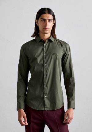 Olivenfarbene Button-Up-Bluse aus glattem Stoff, mit spitzem Kragen, langen Ärmeln und dezentem Logo auf der Brust. Kontrastreiche Knöpfe unterstreichen das Design.
