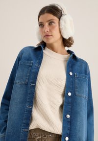 Camicia di jeans con lavaggio blu, chiusura a bottoni, taschino sul petto; maglione cremoso testurizzato sotto, abbinato a pantaloni beige e cuffie bianche soffici.