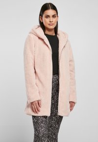 Cappotto in pelliccia artificiale di colore rosa chiaro con cappuccio, dotato di chiusura a zip frontale e maniche lunghe. Materiale morbido e testurizzato con design di lunghezza media.