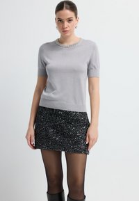 Grå kortærmet top med en glitrende perlekrave, stylet med en sort paillet miniskirt. Glat tekstur og tætsiddende design.