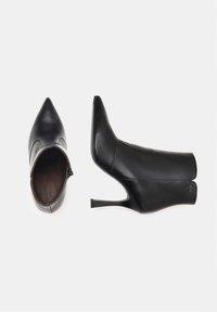 Bottines en cuir noir avec un bout pointu et un talon aiguille fin. Présente un design élégant et une fermeture éclair sur le côté. Texture lisse.