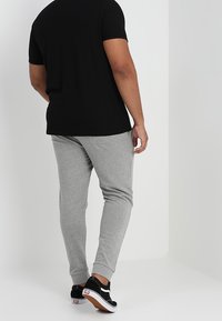 Camiseta negra de manga corta combinada con pantalones de chándal gris claro y zapatillas negras, con un diseño sencillo y tela suave.