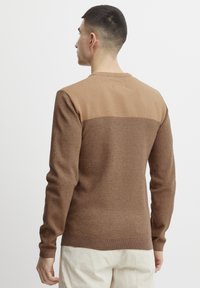 Bruine trui met een gestructureerd bovenstuk, een glad onderstuk, lange mouwen en een ronde halslijn. Kenmerkt zich door een warme kleurenschema.