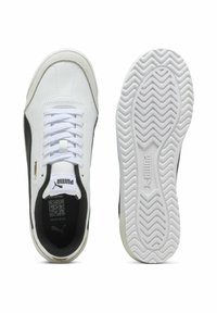 Baskets blanches en cuir avec des accents noirs, dotées d'une semelle texturée, de lacets blancs et d'un logo sur le côté et sur la languette.