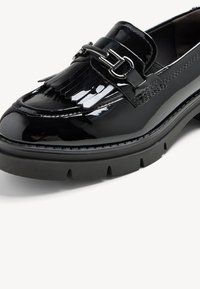 Mocassin verni noir avec un détail à frange et un matériel argenté. Semelle épaisse noire avec des rainures pour une meilleure adhérence. Design à bout arrondi.