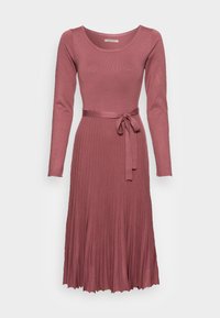 Robe en tricot rose poussiéreux à manches longues, avec col rond, jupe plissée et ceinture en tissu assortie nouée à la taille.