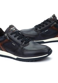 Sneakers in pelle nera con accenti marroni tono su tono, dotati di una zip laterale, lacci rotondi e una suola intermedia bianca. Suola esterna in gomma testurizzata.