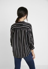 Schwarz gestreifte Bluse mit vertikalen Streifen in unterschiedlichen Breiten, rosa Akzenten, einem gerafften Rücken und Dreiviertelärmeln.