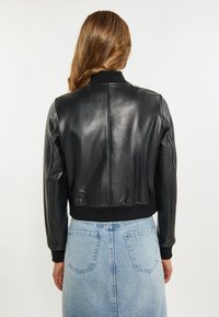 Jacket de bomber din piele neagră cu mansete și tiv cu nervuri, având o textură netedă și un design ajustat. Purtați peste o fustă din denim albastru deschis.