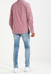 Camisa de manga larga a cuadros rojos y blancos con cuello abotonado, combinada con vaqueros pitillo azul claro y zapatillas blancas.