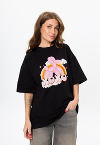 Zwarte oversized t-shirt van katoen, met een kleurrijke ballon-dier grafiek, regenboog en "XOXO" tekst in het wit, op een wolk achtergrond.
