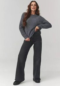 Szary sweter dzianinowy w połączeniu z czarnymi spodniami o wysokim stanie i szerokich nogawkach. Stylizacja charakteryzuje się luźnym krojem i miękką teksturą.
