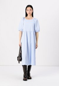 Svijetloplava gingham midi haljina s napuhanim rukavima i kvadratnim izrezom, uparena s visokim smeškim kožnim čizmama i malom crnom torbicom.
