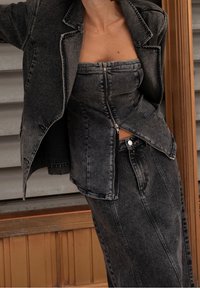 Abbigliamento in denim di lavaggio nero composto da un top aderente con zip, una giacca su misura e una gonna alta coordinata, il tutto con cuciture in evidenza.