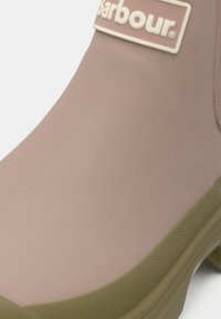 Λαστιχένιο μποτάκι αστραγάλου σε ανοιχτό ροζ με πράσινη σόλα. Διαθέτει υφή φινιρίσματος και ξεχωριστή λευκή ετικέτα με λογότυπο.