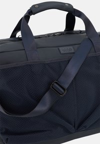 Borsa blu navy con un design elegante, tasche in rete, spallacci robusti e superficie testurizzata. Include una toppa con il logo del marchio sulla parte anteriore.