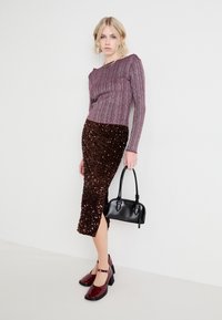 Haut mauve à manches longues en ribbes associé à une jupe midi brune pailletée avec une fente sur le côté. Sac à main noir et chaussures à talons bordeaux.