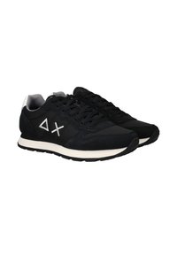 Schwarze Low-Top-Sneaker mit weißen Sohlen und weißen Delta- und X-Symbolen an den Seiten, ausgestattet mit schwarzen Schnürsenkeln und grauem Innenfutter.