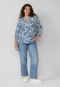 Witte top met blauw bladerenpatroon, V-halslijn, driekwart mouwen. Gepaarde met lichtblauwe wijde jeans en witte sneakers.