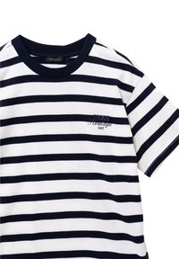 Camiseta a rayas de algodón blanca y azul marino. Cuenta con mangas cortas, un cuello redondeado y bordado en el lado izquierdo del pecho con "Heritage 1987."