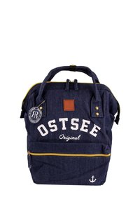 Sac à dos en denim bleu marine avec le texte blanc "OSTSEE Original", des fermetures éclair dorées, des accents en cuir brun et un détail d'ancre en bas.