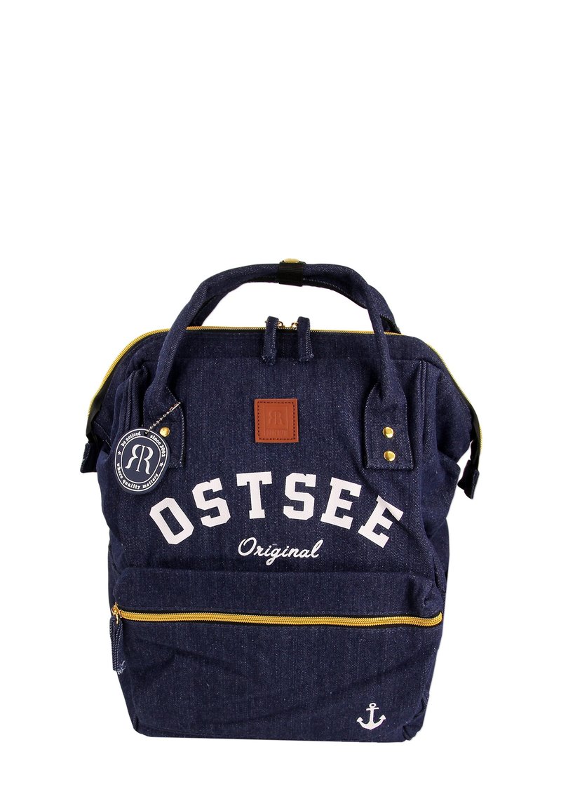 Sac à dos en denim bleu marine avec le texte blanc "OSTSEE Original", des fermetures éclair dorées, des accents en cuir brun et un détail d'ancre en bas.