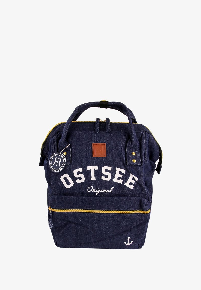Sac à dos en denim bleu marine avec le texte blanc "OSTSEE Original", des fermetures éclair dorées, des accents en cuir brun et un détail d'ancre en bas.