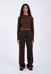 Hnědý žebrovaný top s dlouhým rukávem, tmavé džíny s vysokým pasem, černý opasek s cvočky, hnědé nazouvací boty, nošeno s rovným střihem nohavic.