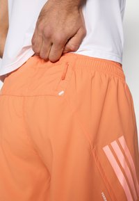 Ανδρικό ελαφρύ πορτοκαλί αθλητικό σορτς με ελαστική μέση, πλαϊνή τσέπη και τρεις ροζ ρίγες στο κάτω μέ�ρος του ποδιού. Λεία υφή.