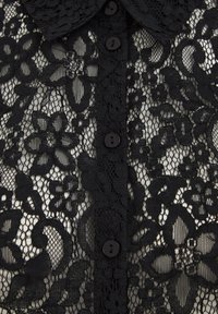 Must mustriga pluus, millel on lillemustrid, nööbid ees ja krae. Tekstuuriga, siidine kangas näitab keerukust ja disaini.