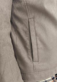Jachetă gri din suede artificial, în prim-plan, cu un buzunar lateral, cusături curate, textură netedă și croială ajustat�ă.