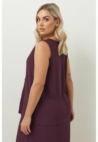 Ärmleös topp i strukturerad mörk lila tyg med ett zickzackmönster, med lös passform och rundad ryggdesign.