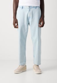 Light blue denim jeans with a loose fit, five-pocket design, and contrast stitching. Worn with beige sneakers.