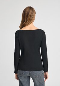 Maglietta nera a maniche lunghe con scollatura a girocollo, realizzata in tessuto morbido. Il design presenta una silhouette aderente e un orlo curvo sul retro.