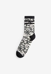 Eine einzelne schwarz-weiße Socke mit Leopardenmuster, schwarzer Spitze, Ferse und Bündchen auf weißem Hintergrund.