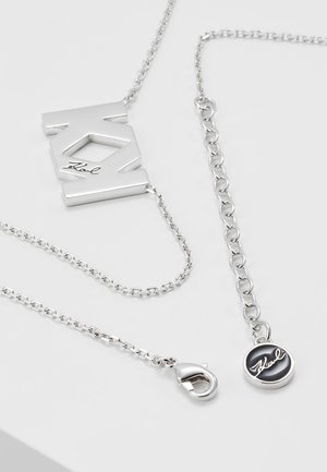 Stříbrný náhrdelník s geometrickým přívěskem s vyřezávaným designem a vyrytým podpisem "Karl", plus zapínání a značková kulatá visačka.