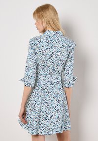 Blau-weißes Blumenkleid mit Kragen, Dreiviertelärmeln und ausgestelltem Rock. Das Muster zeigt kleine Blätter in unterschiedlichen Schattierungen.