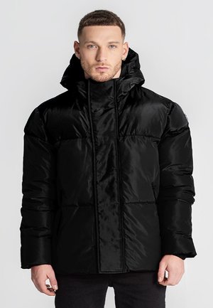 Chaqueta tipo puff negra con textura brillante y suave, cuello alto y cremallera frontal, con acolchado horizontal y bolsillos laterales.