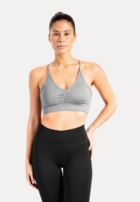 Brassière de sport grise avec un devant froncé, des bretelles réglables et une texture extensible et lisse, associée à un legging noir taille haute.
