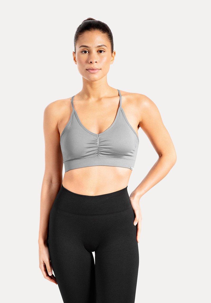 Brassière de sport grise avec un devant froncé, des bretelles réglables et une texture extensible et lisse, associée à un legging noir taille haute.