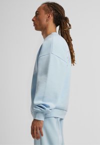 Hellblaues Sweatshirt mit lässiger Passform, gerippten Bündchen und Saum. Weicher Stoff; enthält ein dezentes Logo auf der Rückseite in der Nähe des Halsausschnitts.