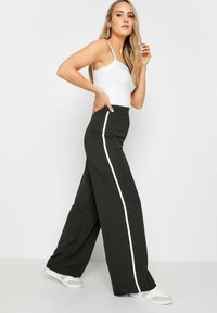 Pantalons larges taille haute noirs avec une bande latérale blanche, en tissu doux en mélange de coton. Associés à un débardeur blanc ajusté et des baskets.