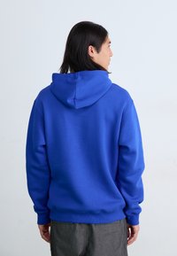 Royal blue hettegenser med snor, ribbestrikkede mansjetter og kant. Glatt tekstur, avslappet passform, og ensfarget bakside uten dekorasjoner.