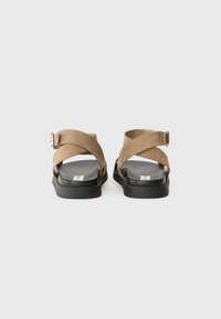 Sandalias de ante marrón con correas entrelazadas, una hebilla ajustable y una suela plana de goma negra. Plantilla suave para mayor comodidad.