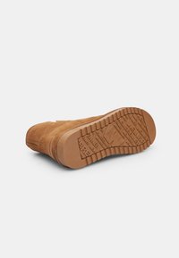 Bocanc din suede maro cu o talpă din cauciuc texturat, având un model de profil aspru și un toc întărit pentru stabilitate.
