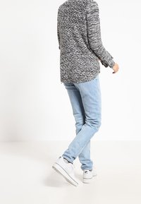 Svart och vit prickig tröja, ljusblå denimjeans och vita sneakers. Tröjan har en avslappnad passform och en längre design bak.